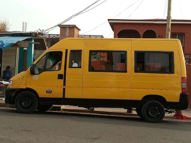 A yellow commercial passenger van, known as a 'trotro', parked on a street in Ghana.