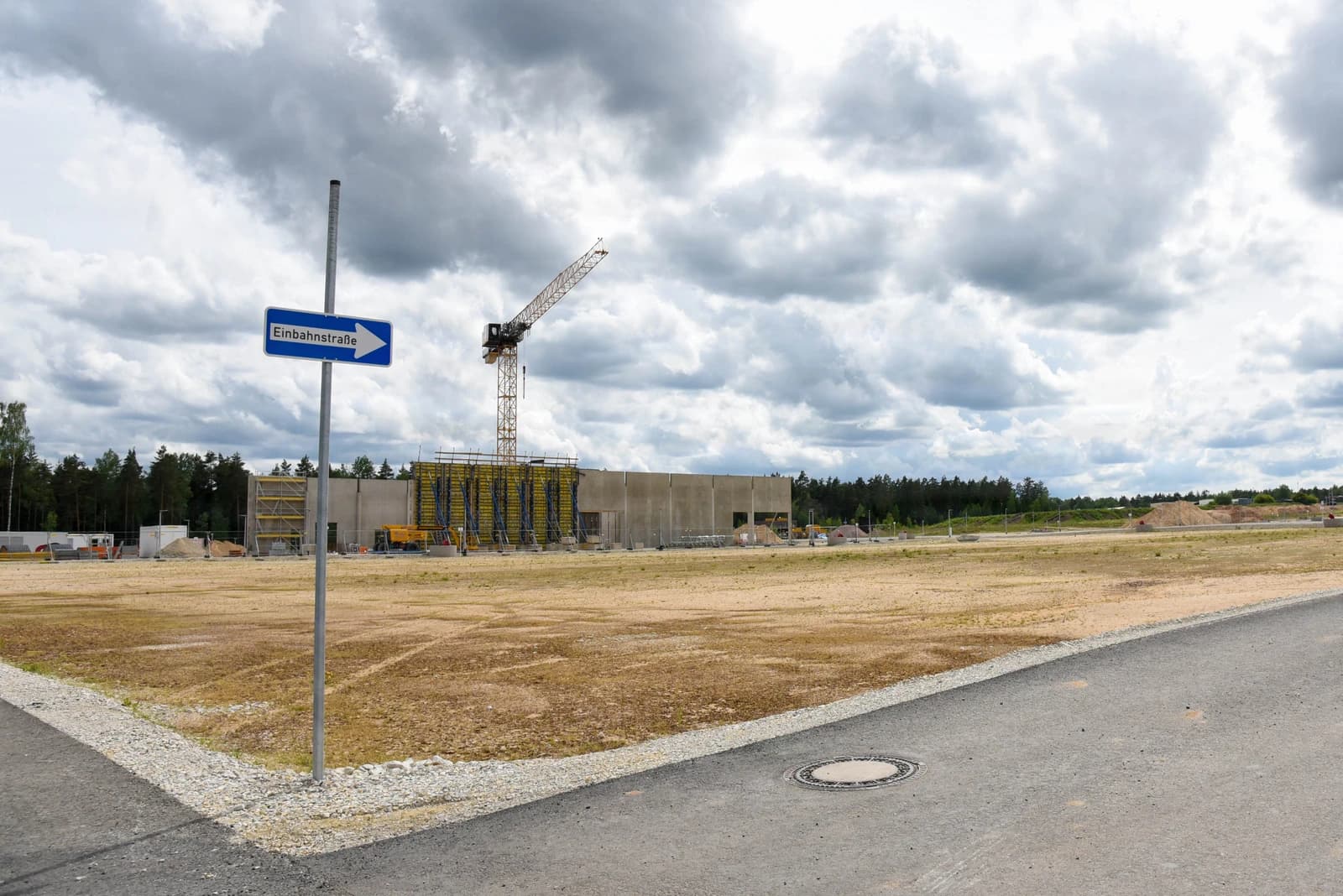 Construction site with an unfinished building, a large crane, and an empty field.
