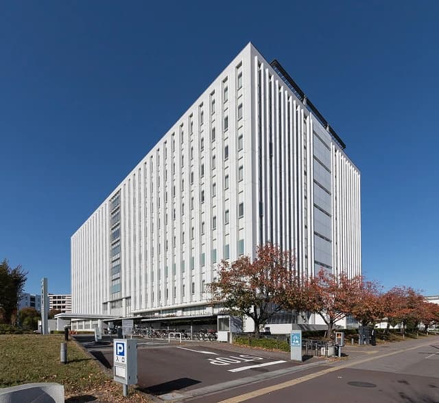 The large, white modern building of the Tokyo District Court Tachikawa branch under a clear blue sky.