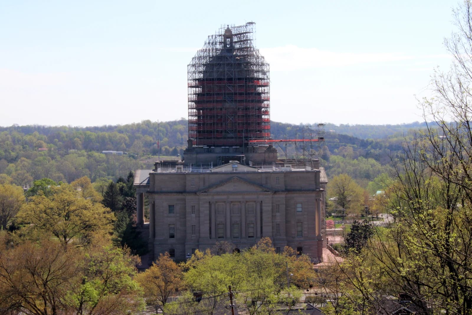 Kentucky State Capitol Building, dome covered in scaffolding, surrounded by green trees.