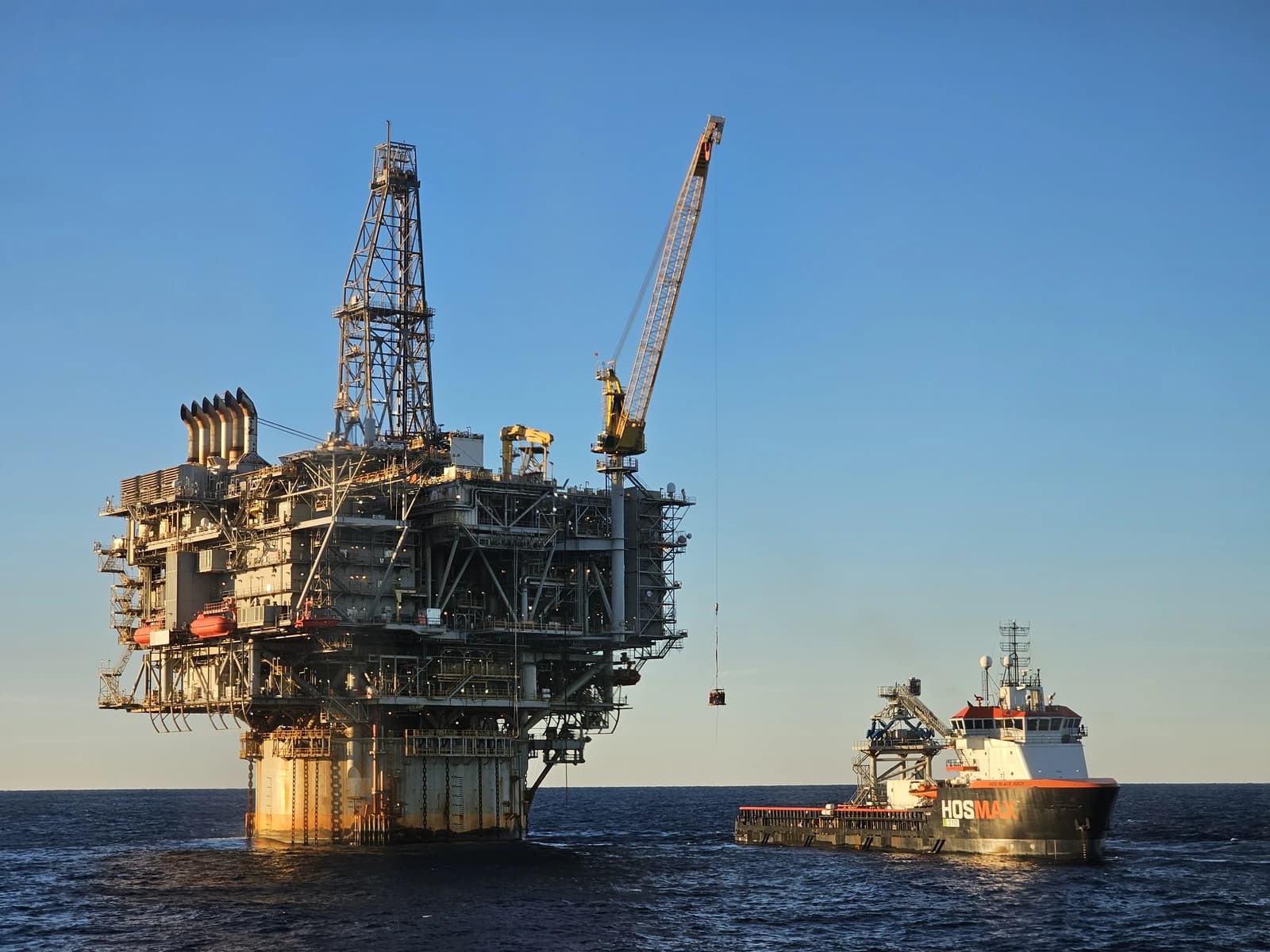An offshore oil platform stands tall in the ocean with a supply vessel nearby.