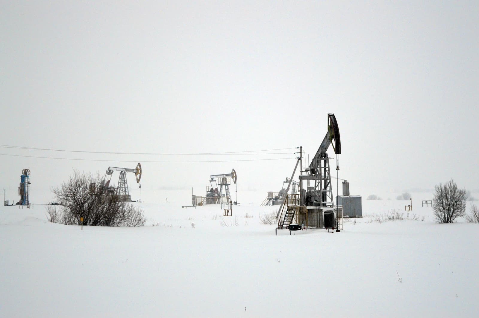 Multiple pumpjacks extracting oil from the ground in a snow-covered field.