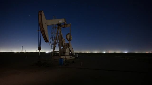 An oil pumpjack operates in a field under a dark night sky.
