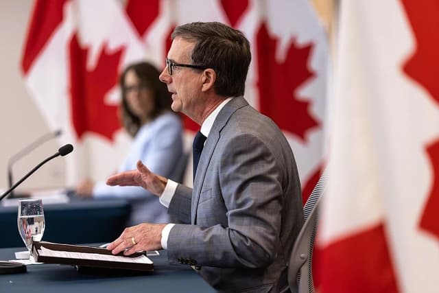 Tiff Macklem, Governor of the Bank of Canada, speaking at a desk with Carolyn Rogers, Senior Deputy Governor, in the background.