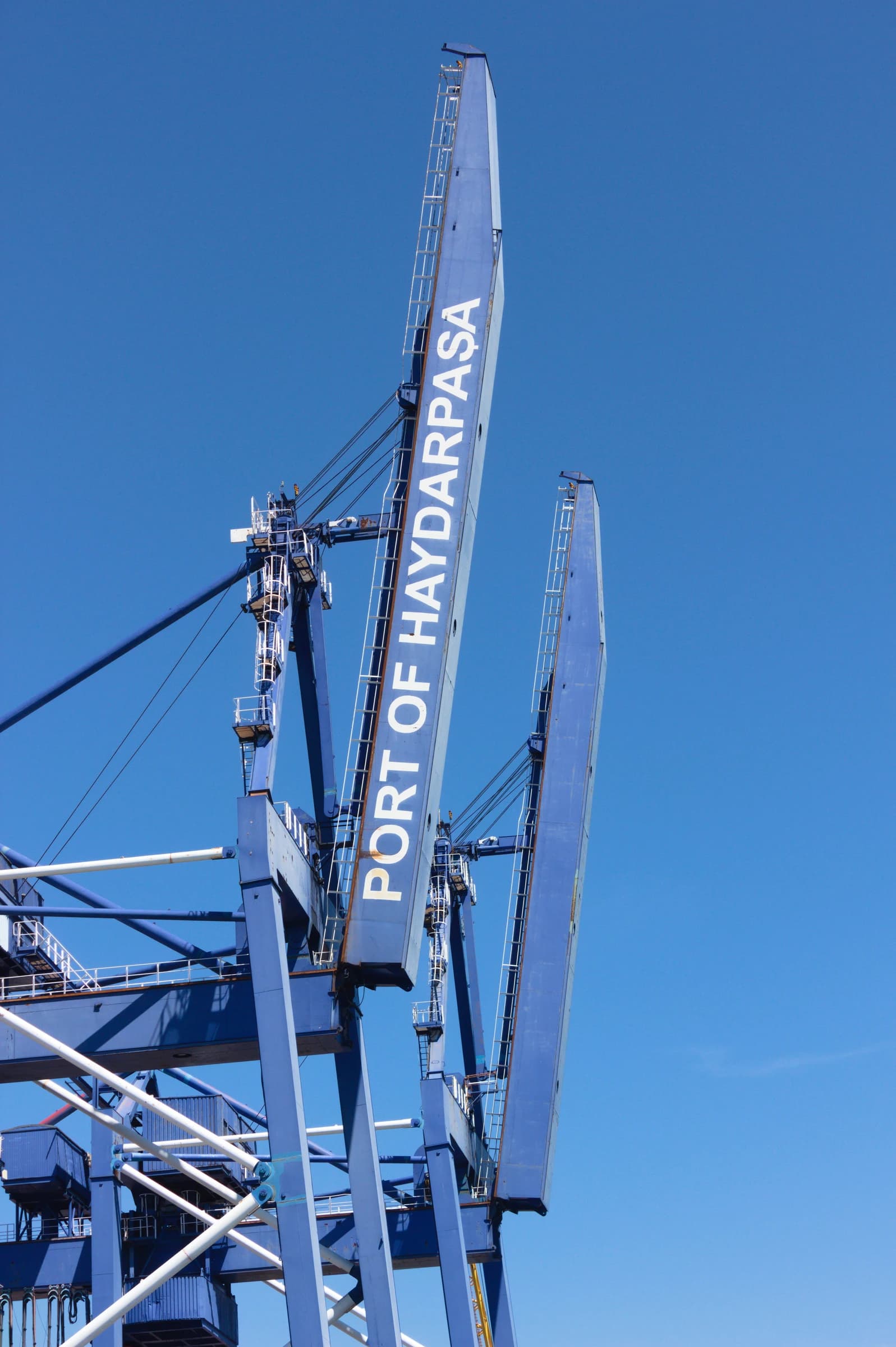 Blue container cranes stand against a clear blue sky at the Port of Haydarpaşa.