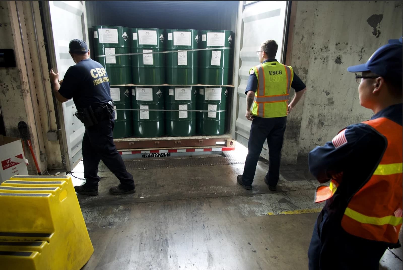 US Customs and Border Protection officers inspect a shipping container with hazardous material barrels.