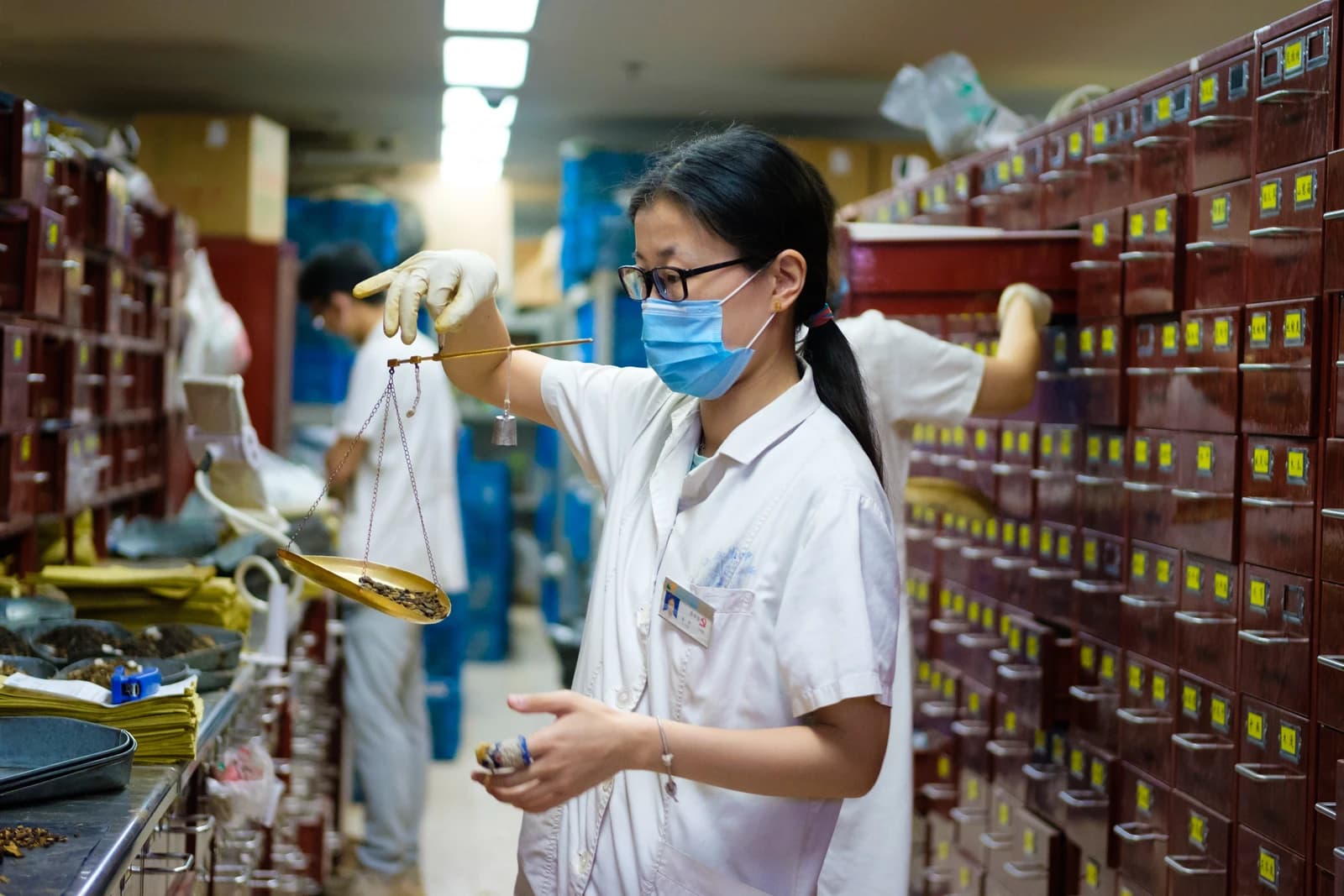 Pharmacist wearing a face mask mixing traditional Chinese medicine with a scale.