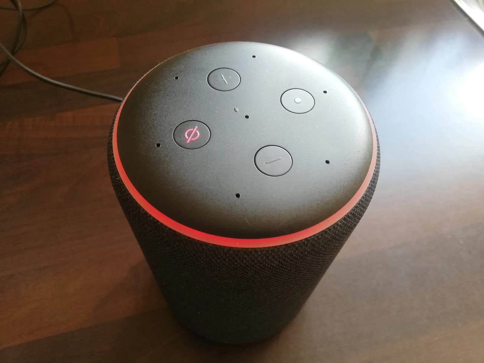 Amazon Echo smart speaker with a flashing red ring on a dark surface.