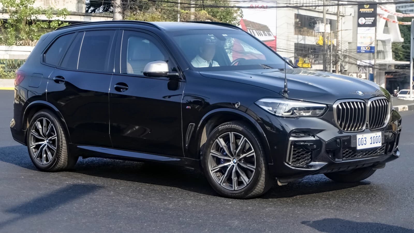 Black BMW X5 M50i F95 SUV driving on a city street.