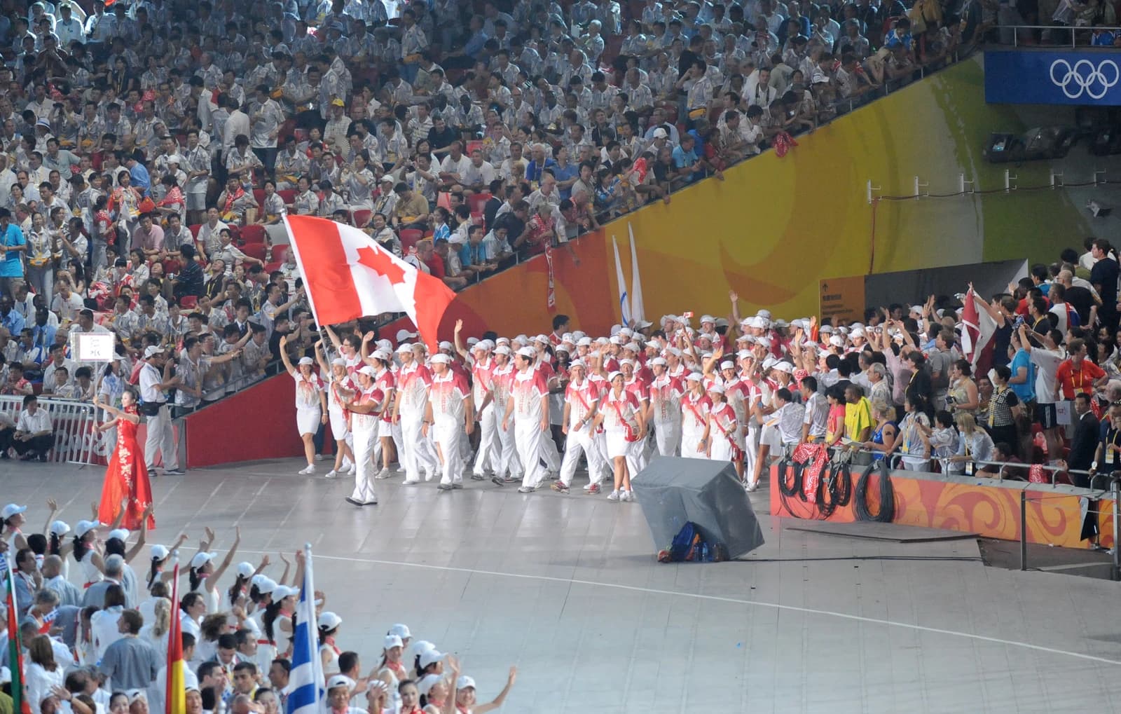 Canadian athletes carrying a large flag enter a stadium filled with spectators.