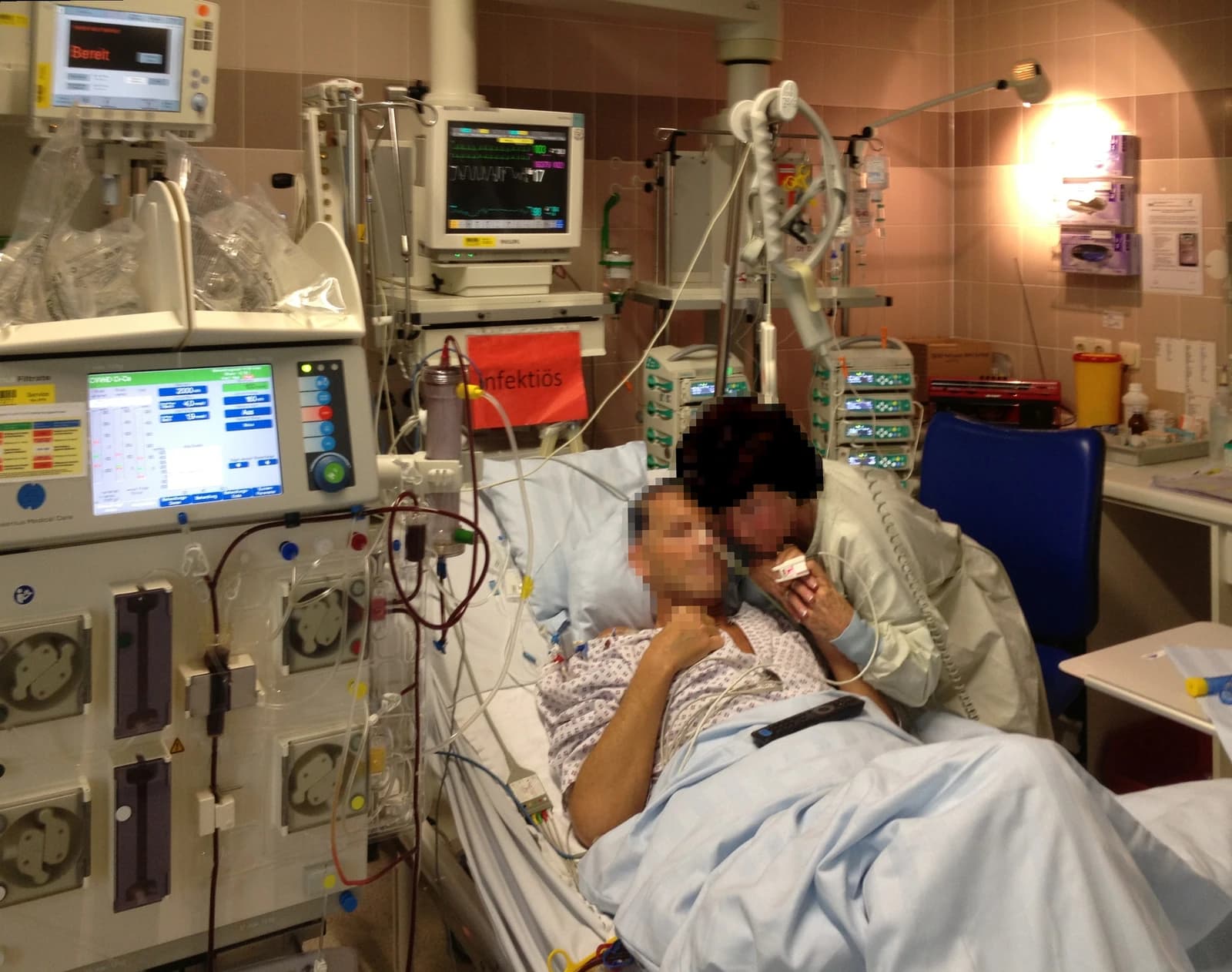 Patient lies in bed with medical equipment and a hemodialysis machine beside them.