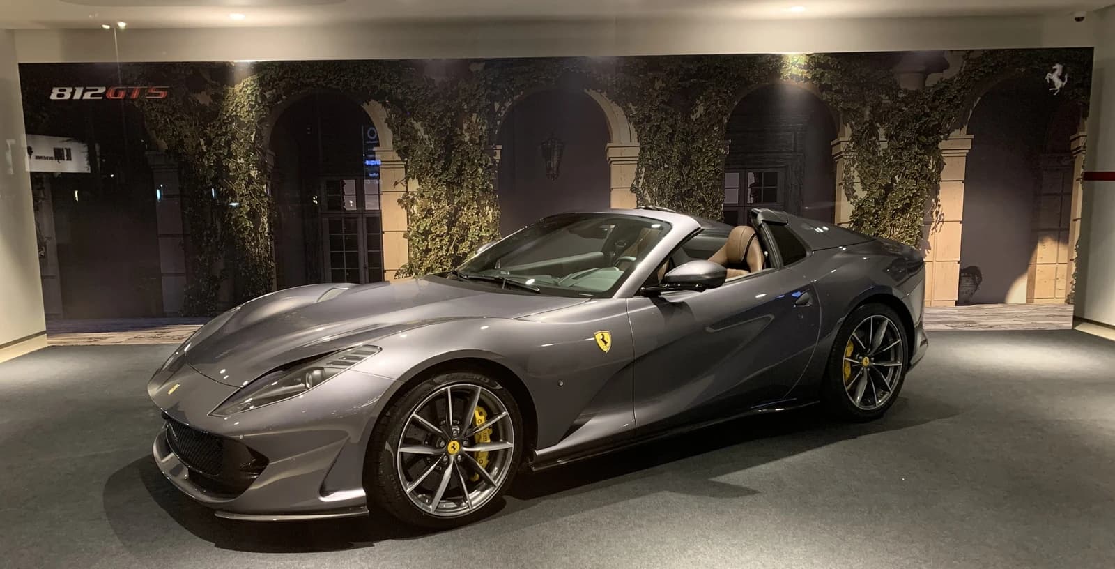 Gray Ferrari 812 GTS sports car with its top down in a showroom.
