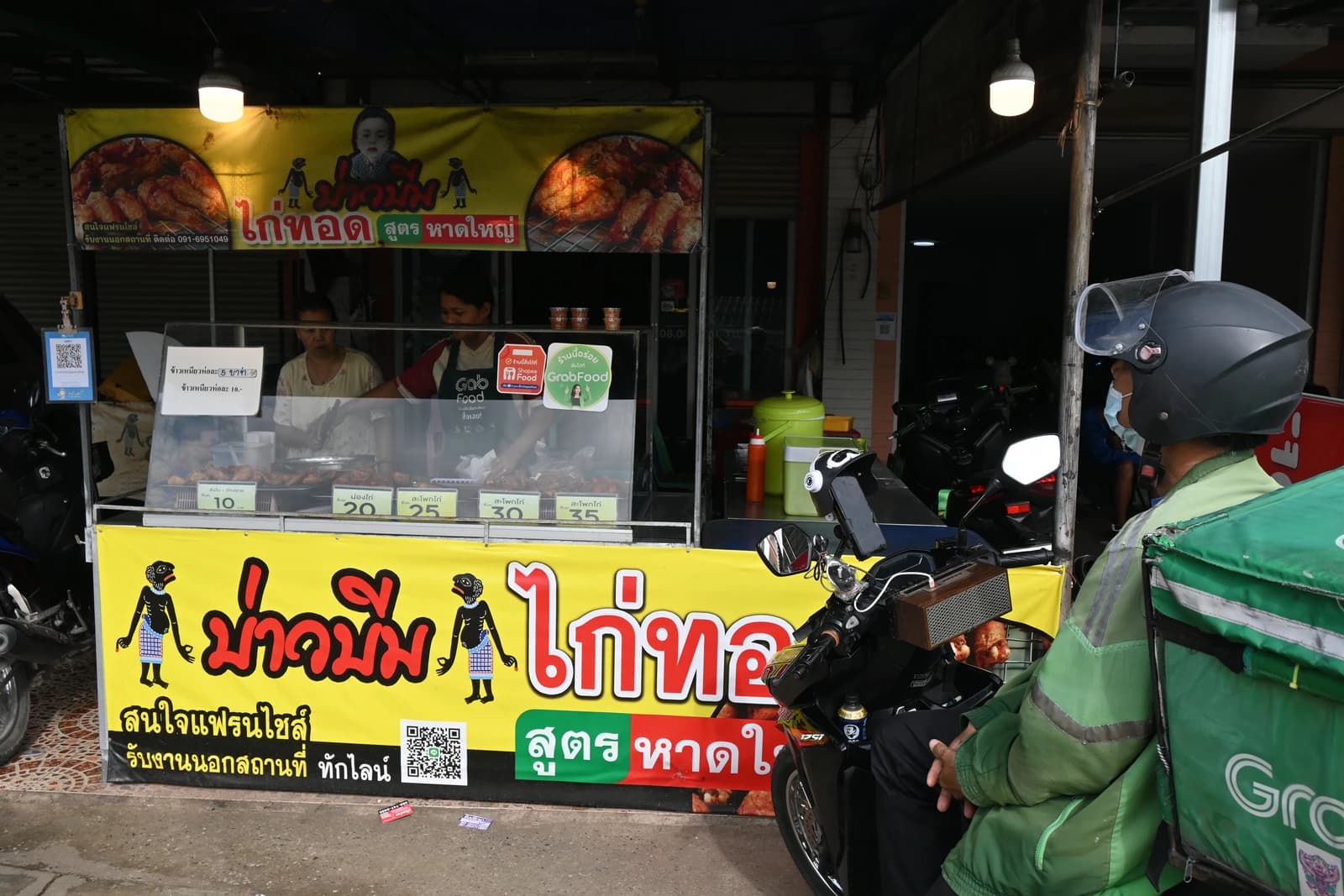 A GrabFood rider waits on a motorbike at a street food stall.