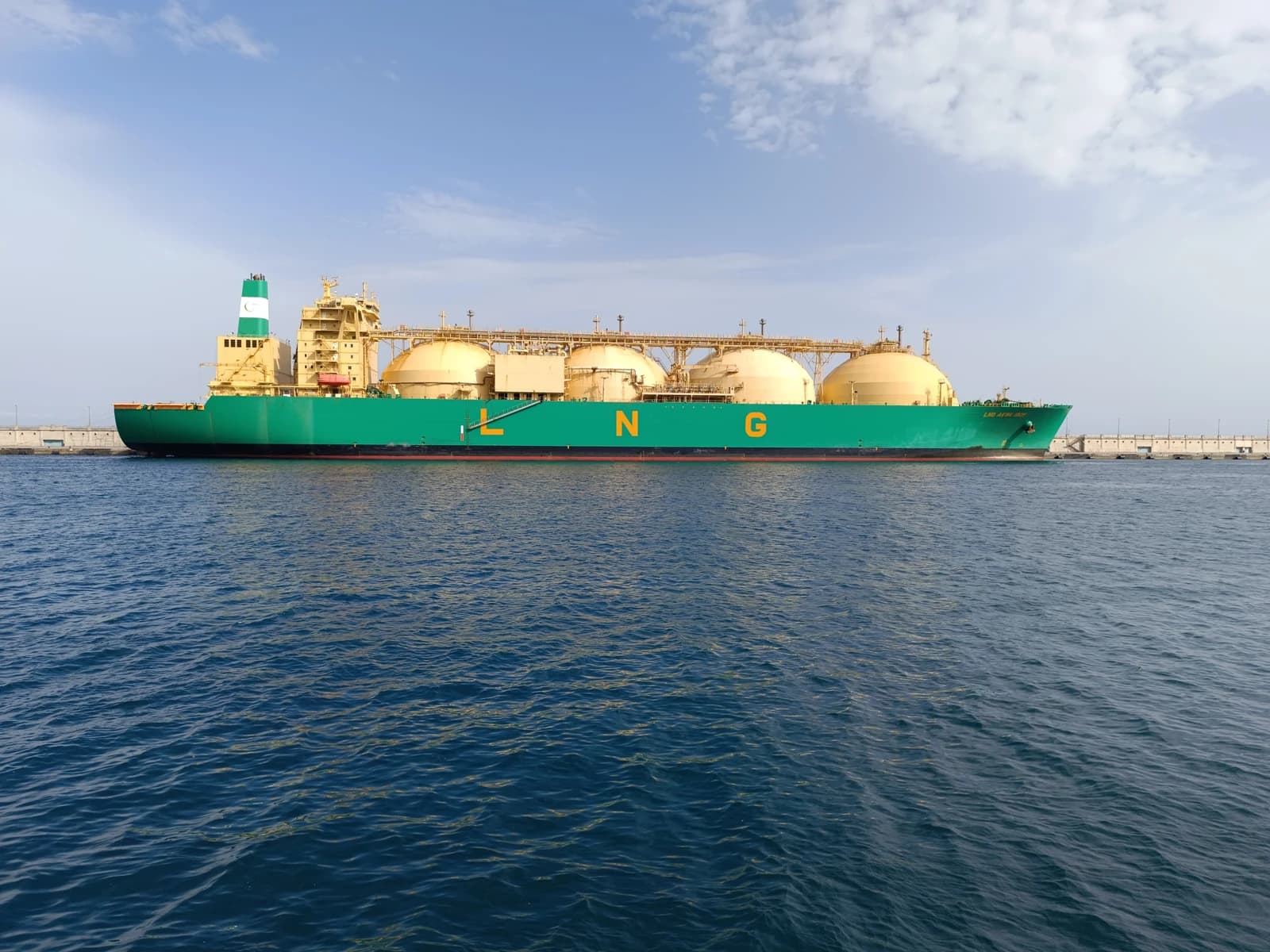 Green and yellow LNG carrier Akwa Ibom in a port with a blue sky.