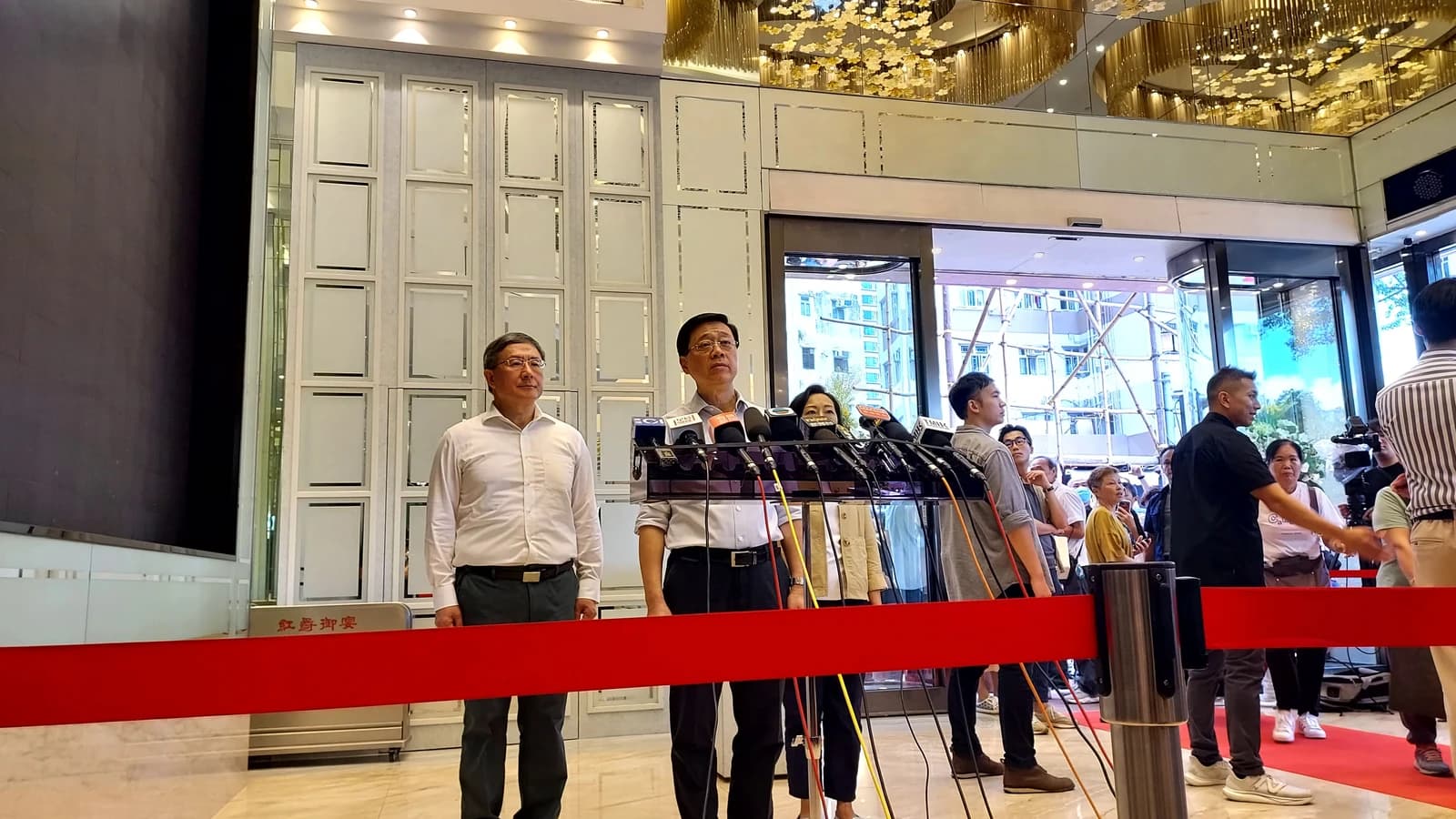 John Lee, Chief Executive of Hong Kong, standing at a podium with microphones during a press conference.