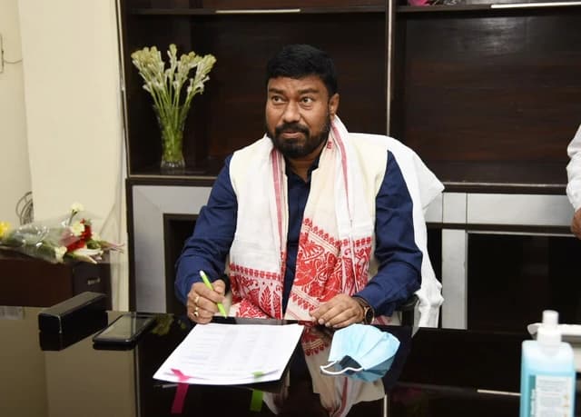 Shri Rameswar Teli, Minister of State for Labour, sitting at a desk and signing documents.