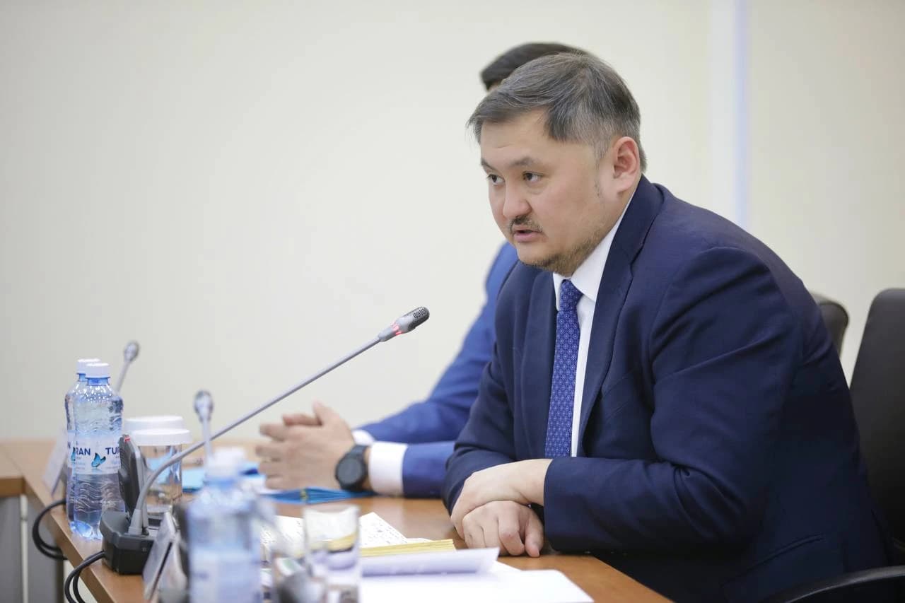 Nurbek Saiasat, Kazakh official, speaking into a microphone at a table.
