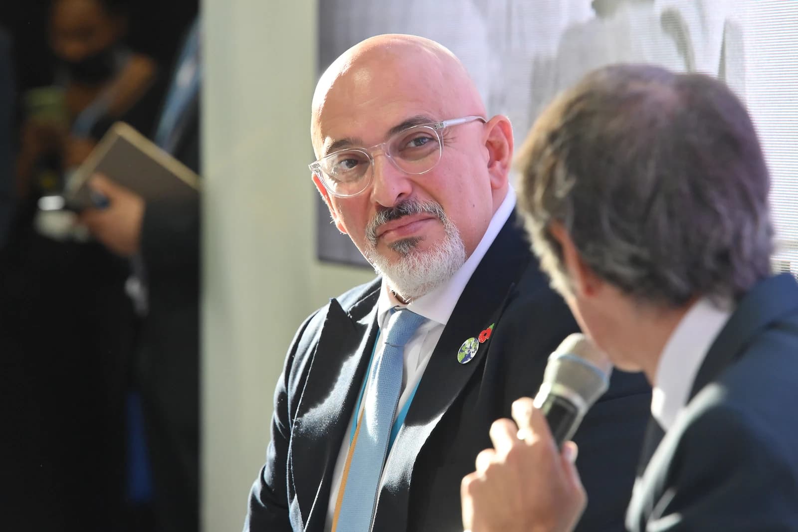 Nadhim Zahawi, British politician, seated and looking towards a speaker holding a microphone.