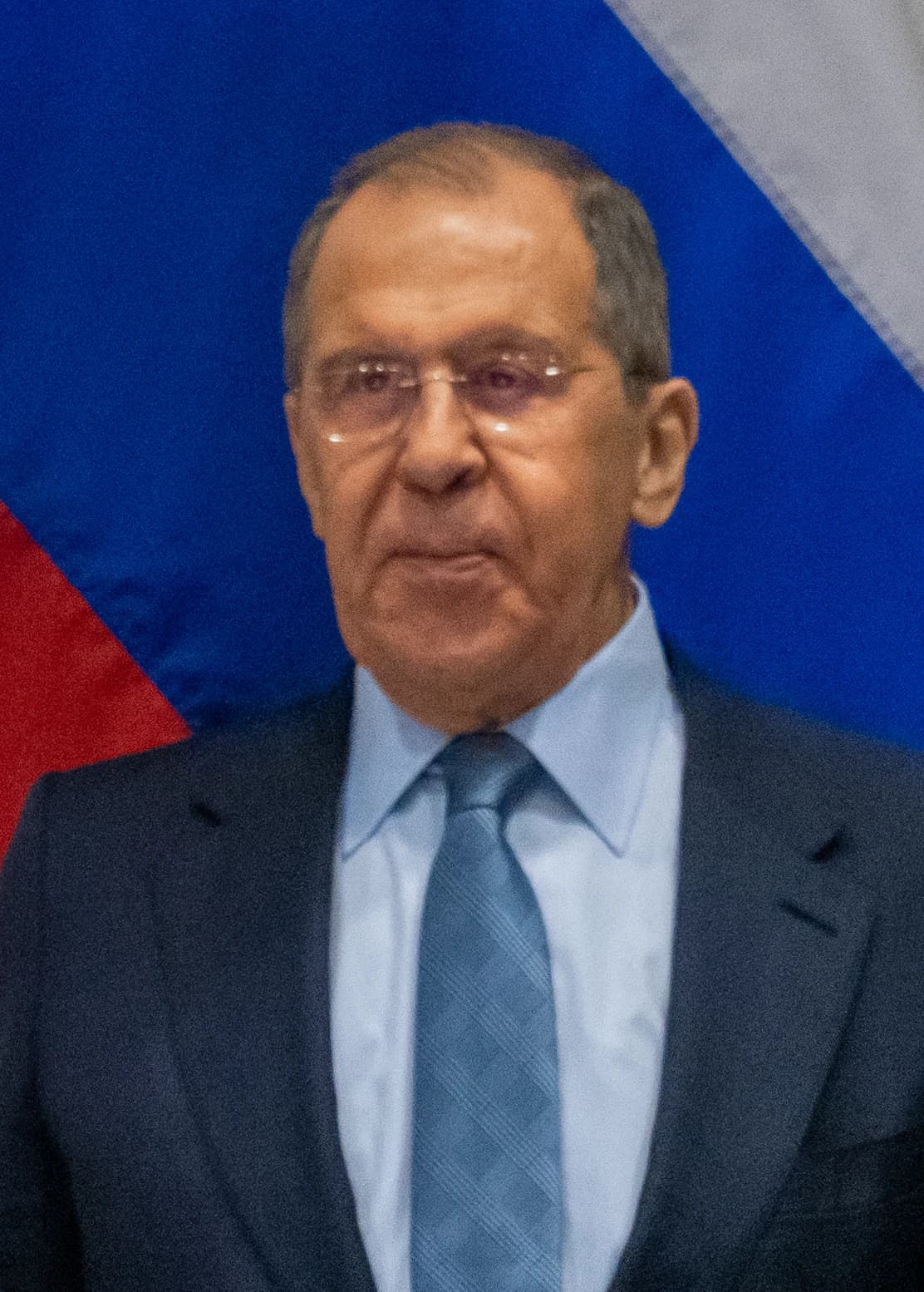 Russian Foreign Minister Sergey Lavrov stands in front of a blue background.