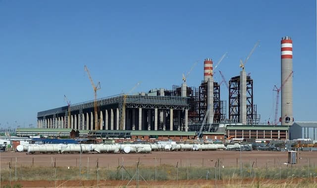 Medupi Power Station construction site with multiple chimneys and cranes under a clear blue sky.