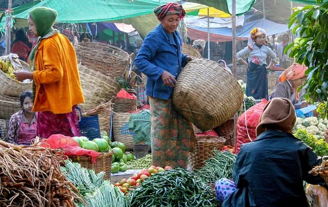 Sellers and customers at a vibrant open-air market with baskets of fresh vegetables.
