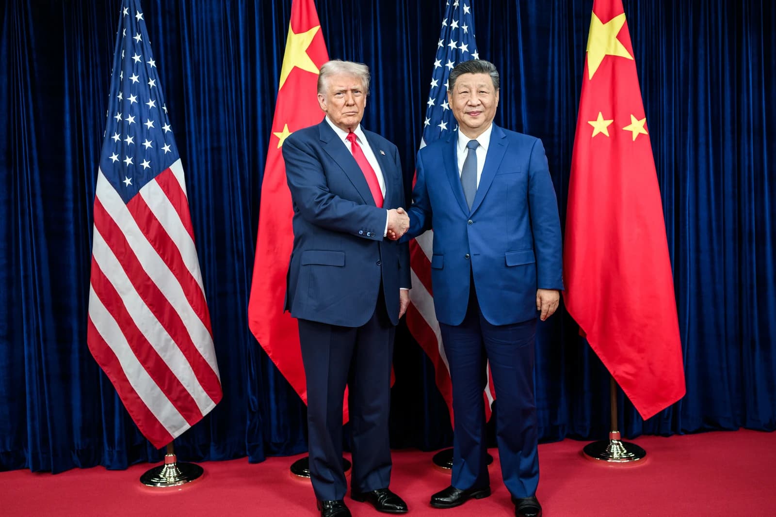Donald Trump and Xi Jinping shake hands in front of US and Chinese flags.