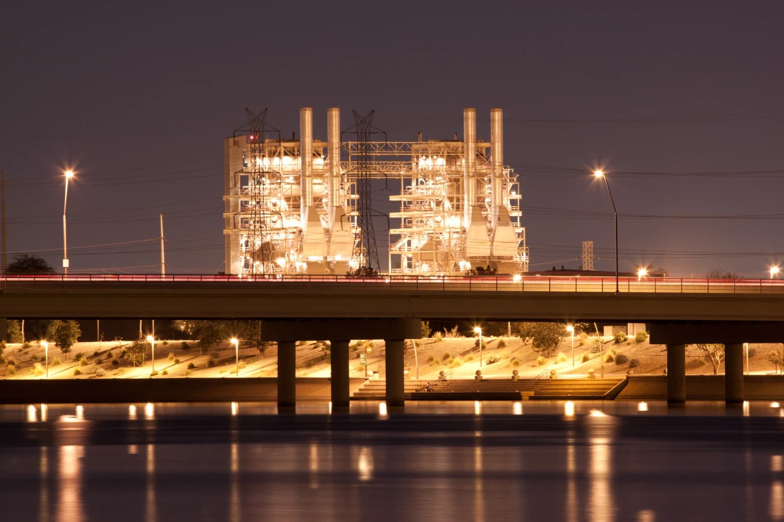 Ocotillo Power Plant at night, with a highway bridge and water reflections in the foreground.