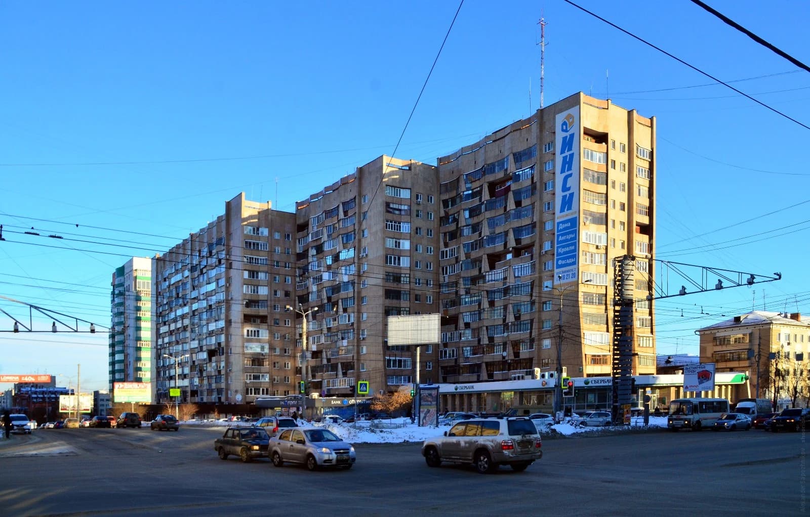 Apartment building with numerous windows and balconies, cars driving on a city street.