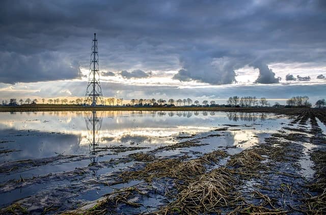 A natural gas extraction tower stands in a flooded field under a dramatic cloudy sky.