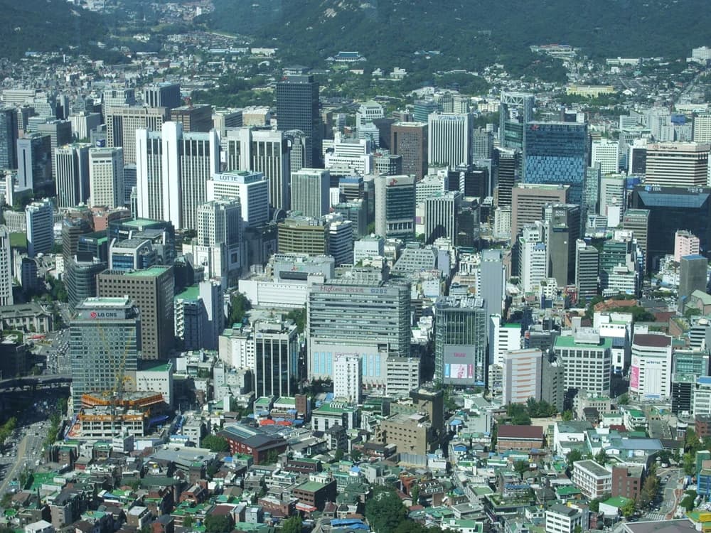Aerial view of Seoul's city core with tall buildings and distant mountains.