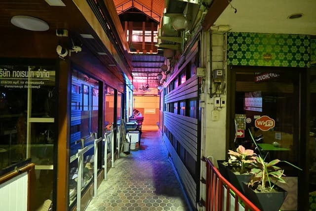 Narrow alleyway with neon-lit shopfronts and reflections on the tiled floor at night.