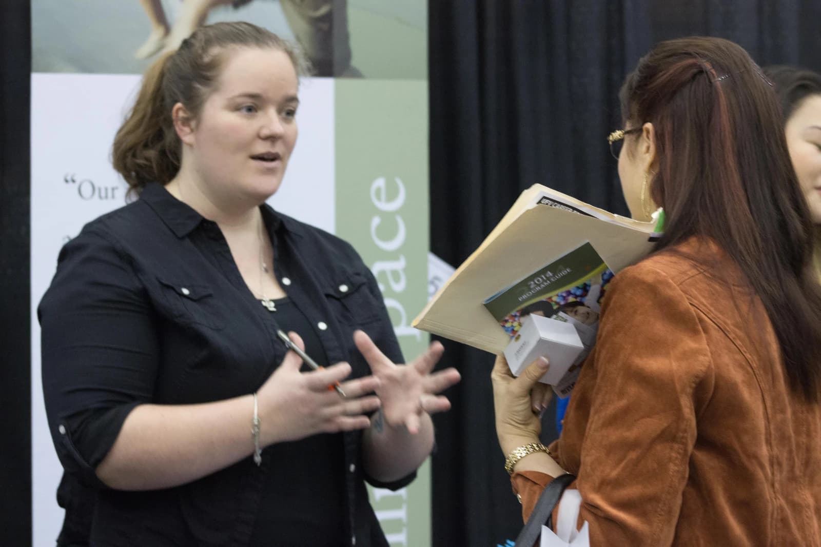 Woman speaks to another woman holding a folder at a career fair.