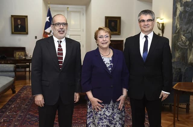 Mario Marcel, President of the Central Bank of Chile, stands between two other individuals indoors.