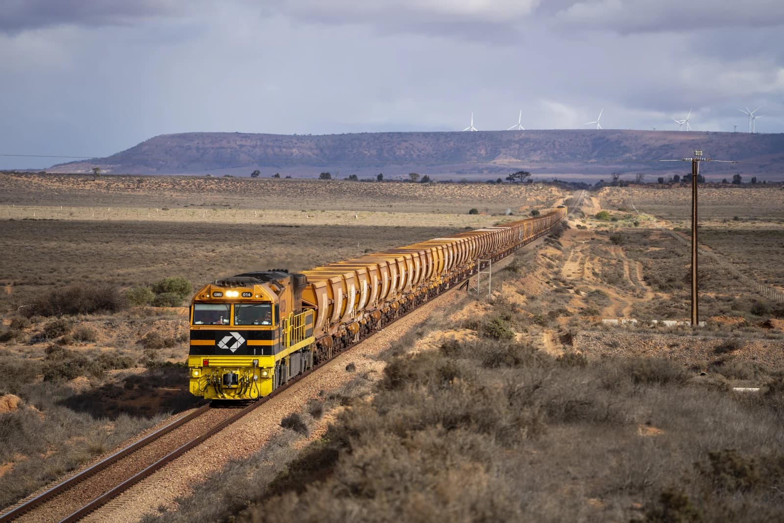 An Aurizon iron ore train on tracks in a dry, sparse landscape.