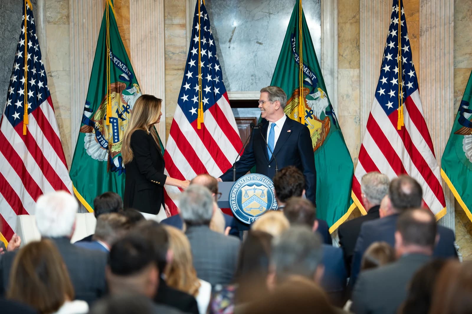 Government officials shake hands at a podium during an event at the Treasury Department.