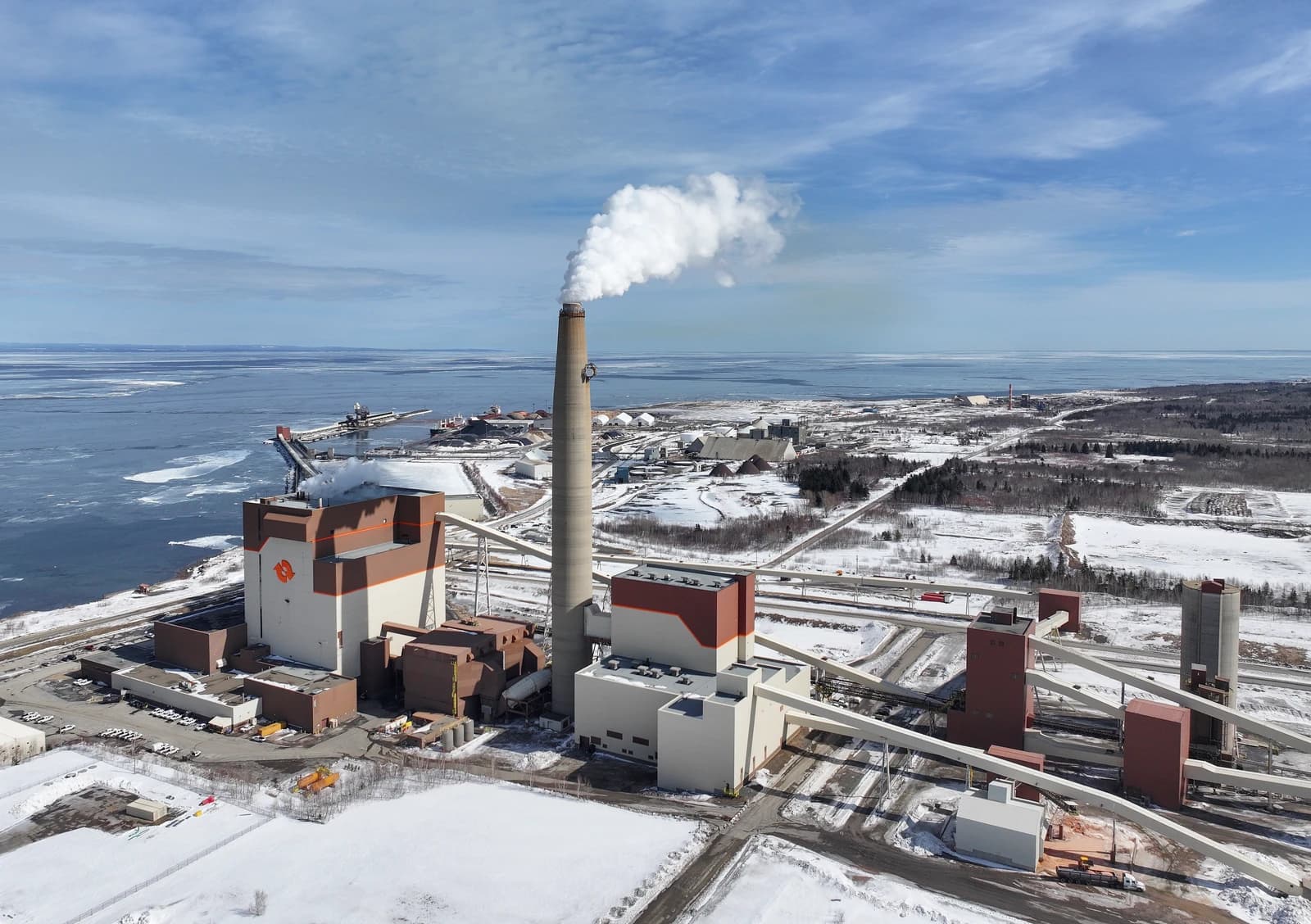 Aerial view of Belledune Generating Station in New Brunswick, Canada, with smoke emitting from tall stack.