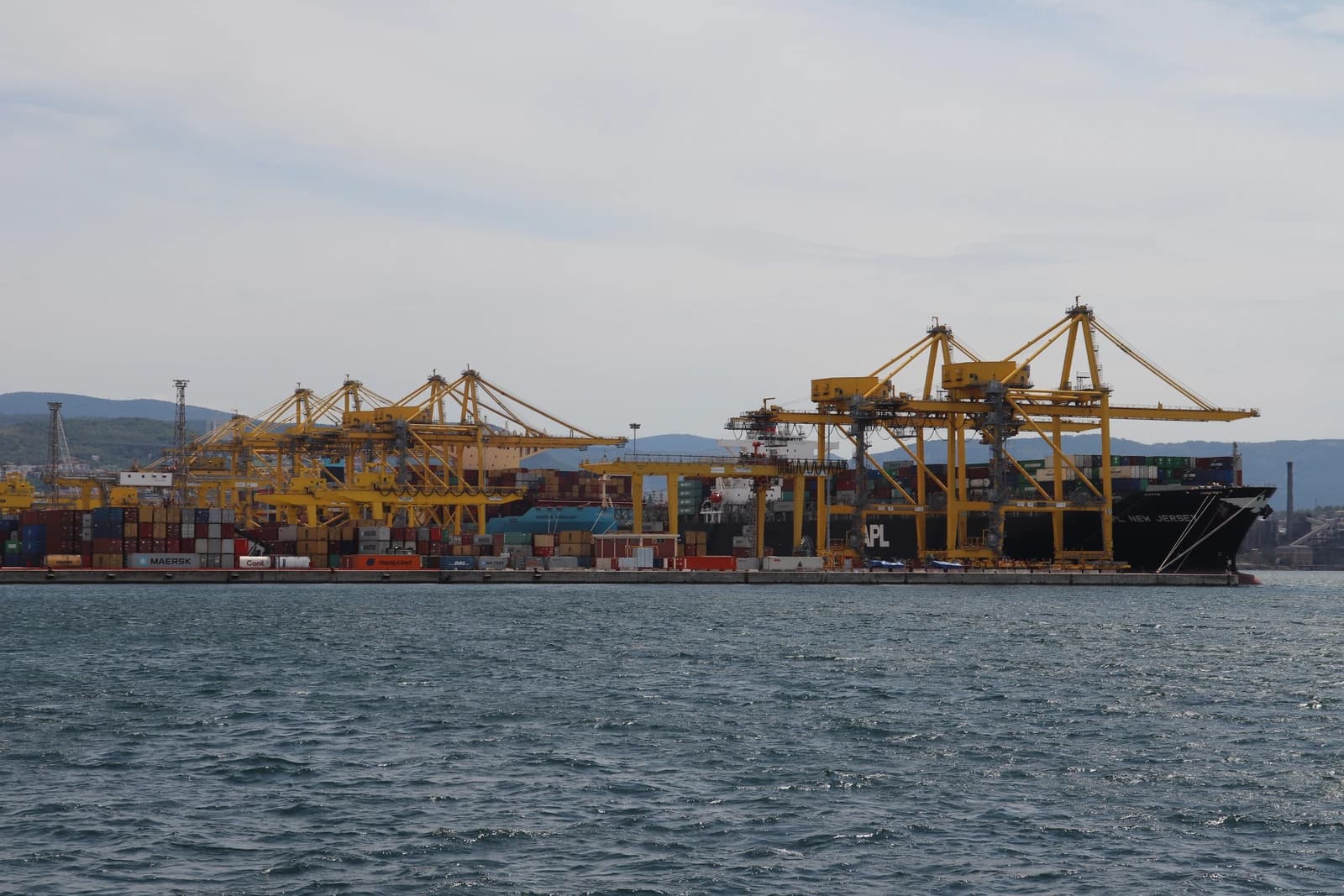 Port of Trieste showing multiple container ships docked with large yellow cranes.