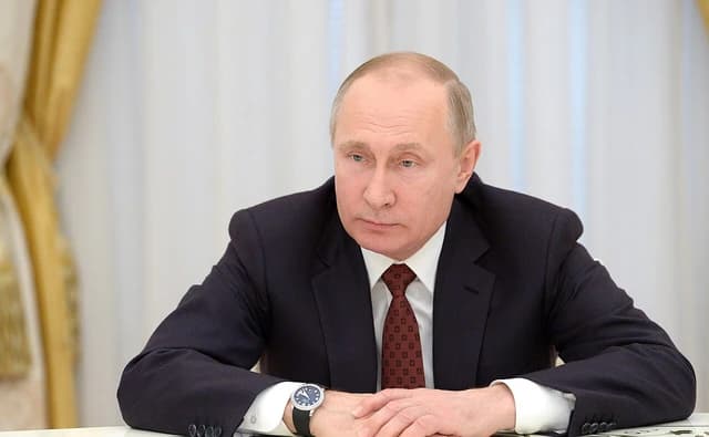 Vladimir Putin, President of Russia, seated at a formal table indoors.