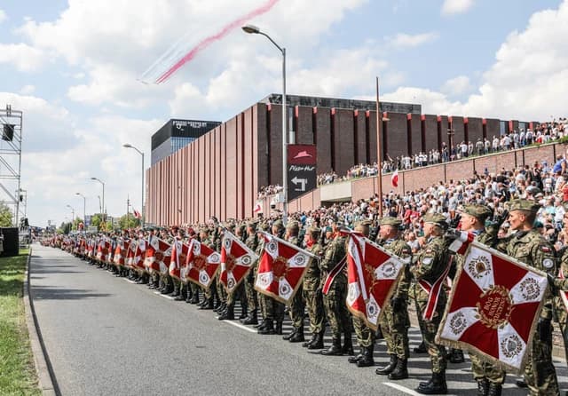 Soldiers in camouflage uniforms standing in formation holding ceremonial flags during a parade.