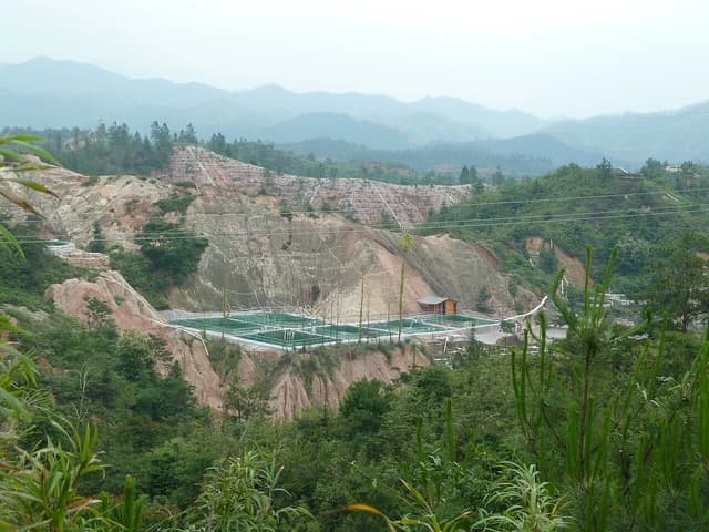 Overview of a rare earth element mining site with terraced hills and processing ponds.
