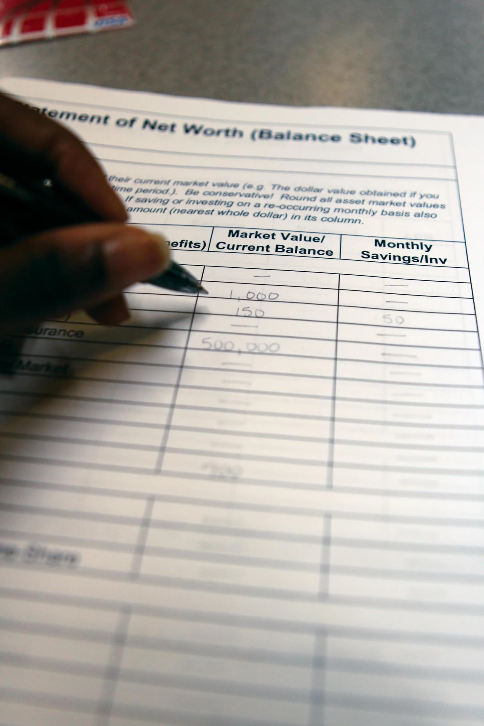 Person's hand writing numbers on a financial statement of net worth form.