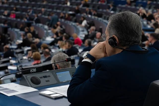 Man wearing headphones and glasses, looking forward at a European Parliament voting session.