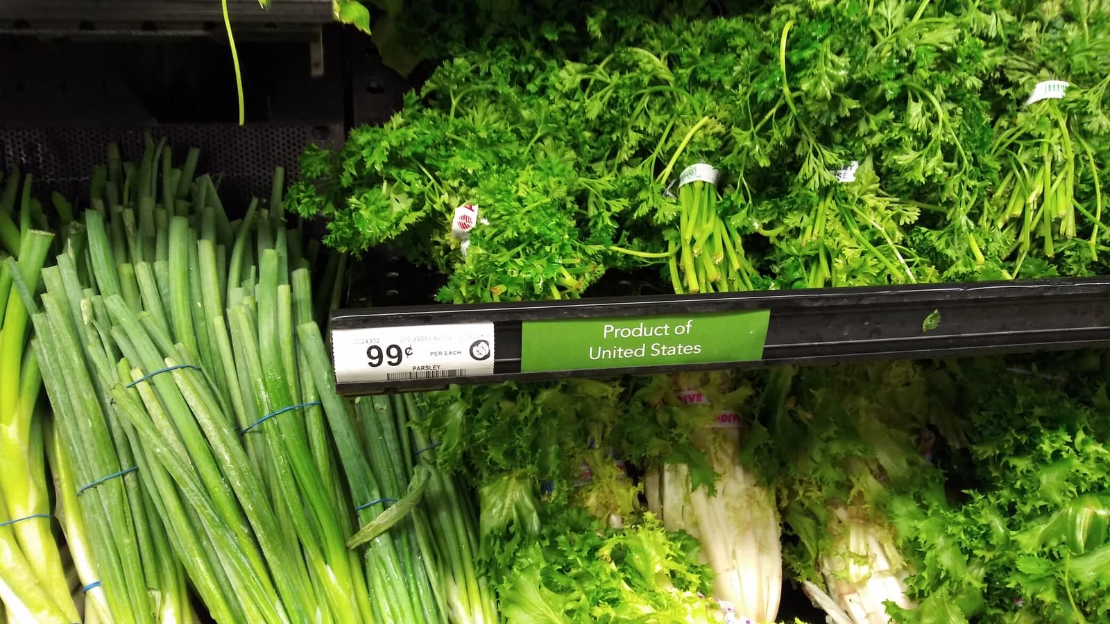 Bundles of parsley and other green vegetables displayed in a supermarket cooler.