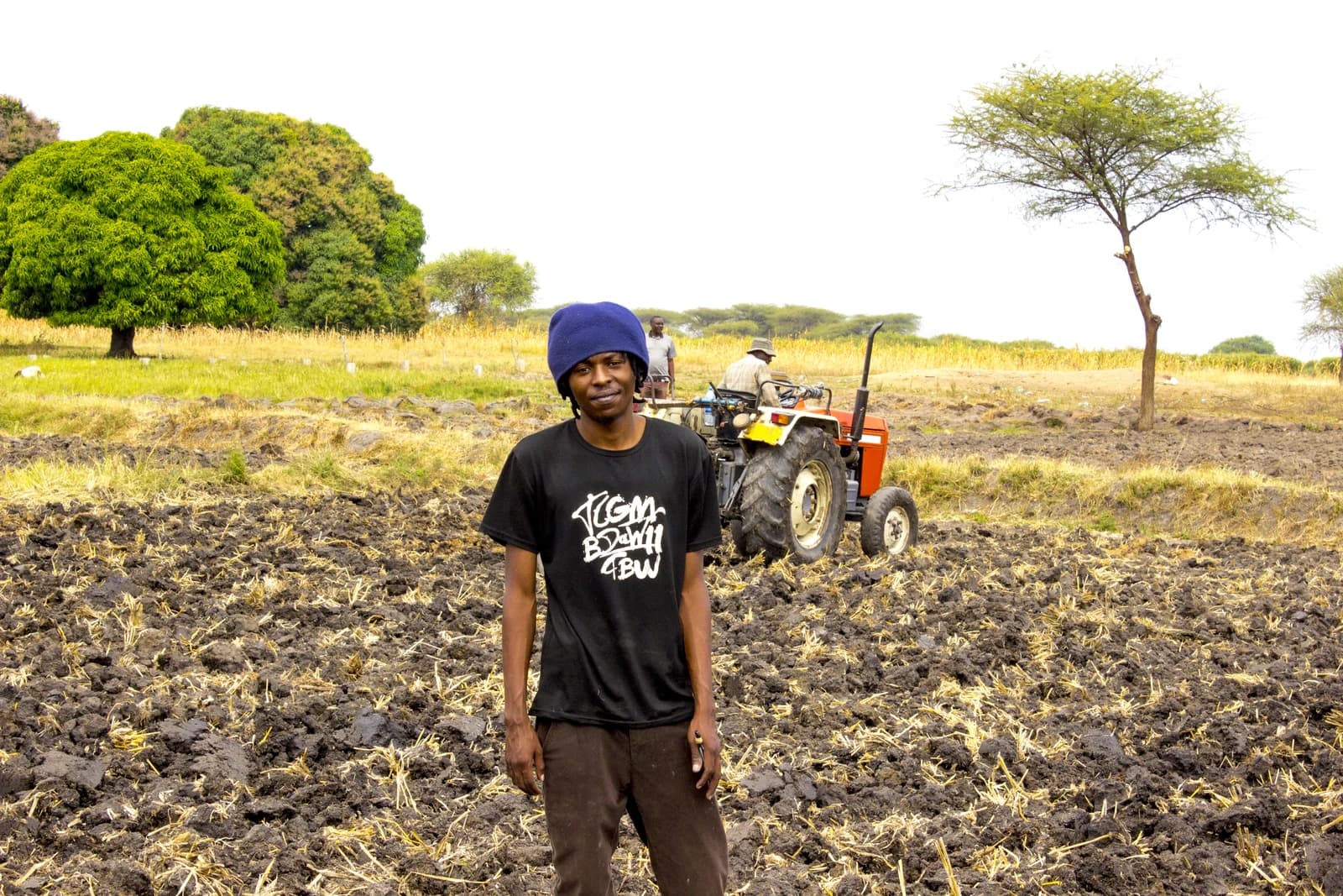 Farmer standing in a recently tilled field with a tractor in the background.