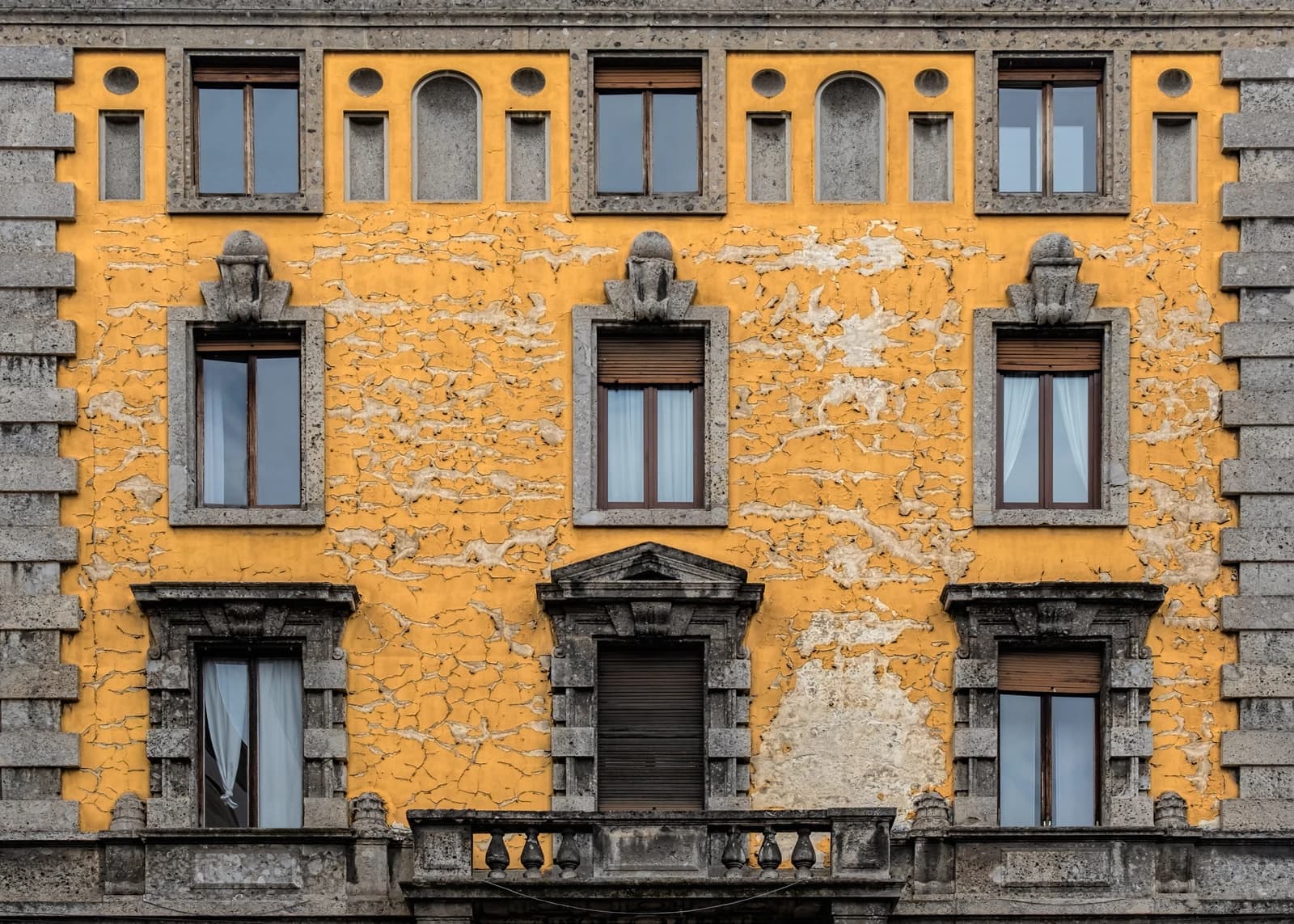 Apartment building in Milan with yellow facade, multiple windows, and stone details.