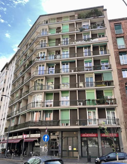 Apartment building with balconies and green shutters in Milan, Italy.