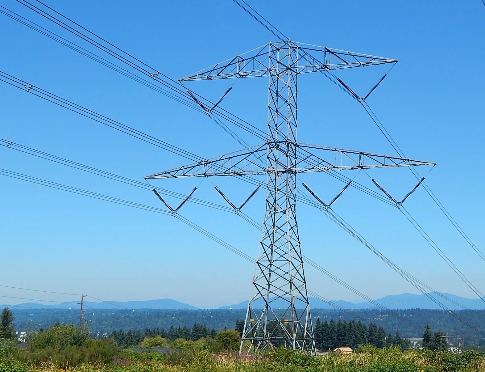High voltage transmission tower with multiple power lines against a clear blue sky.