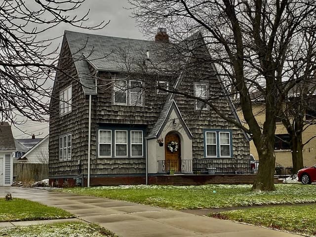 A two-story house with shingled siding and a gray roof, surrounded by bare trees.
