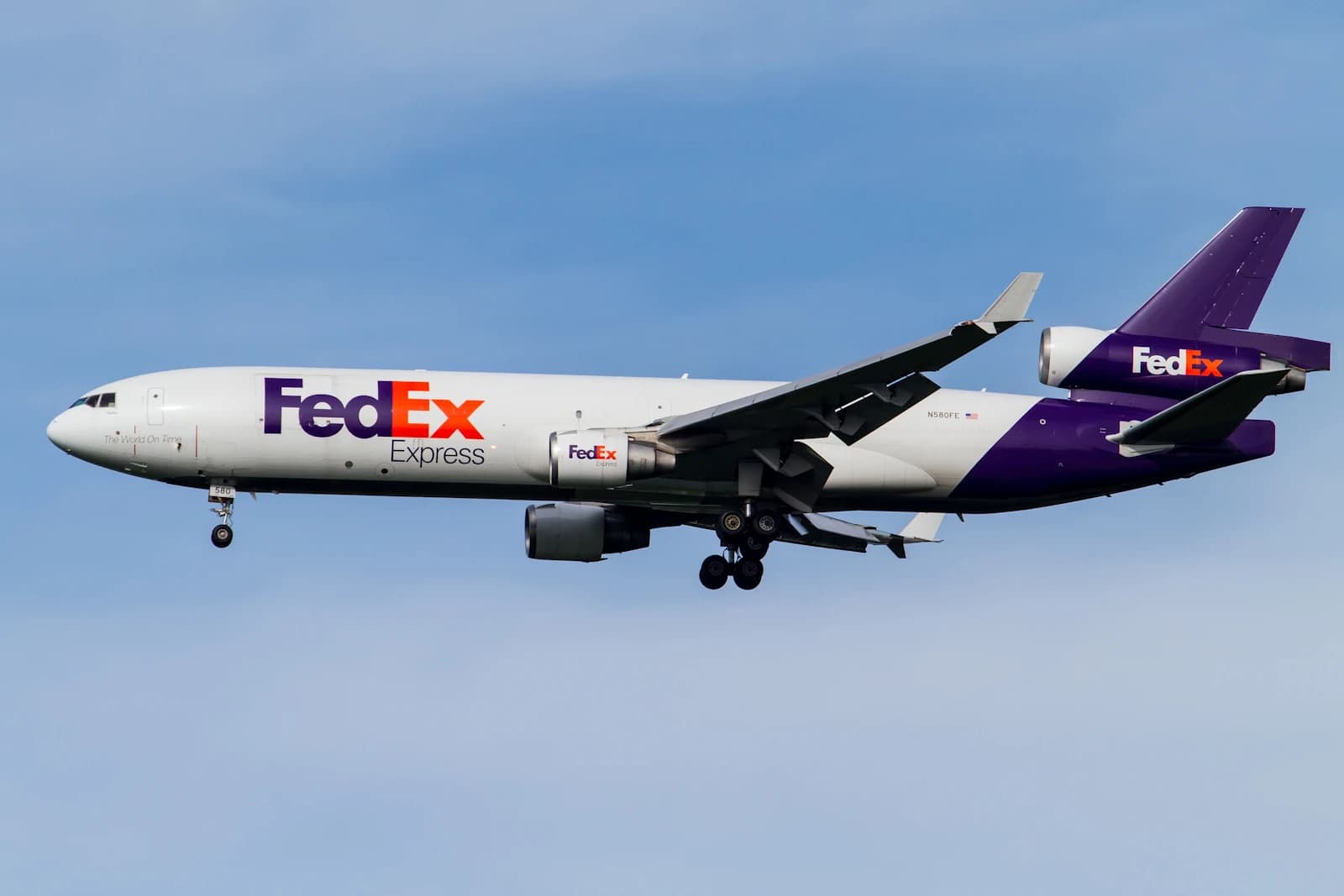 FedEx Express MD-11 cargo plane flying against a blue sky.