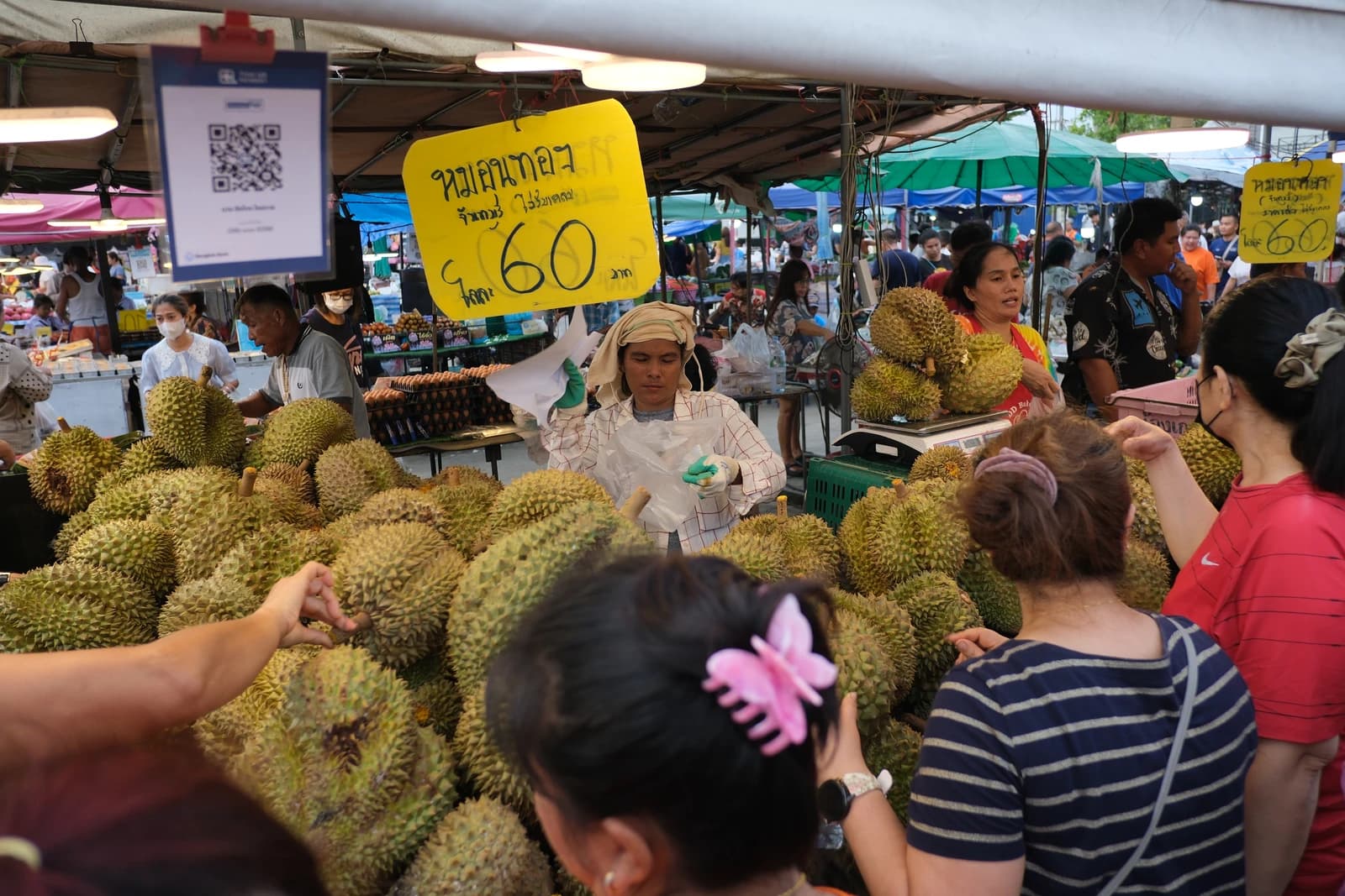 Vendors and shoppers at a market stall piled high with durian fruit.